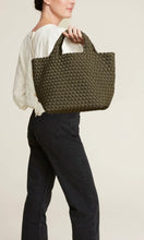 Load image into Gallery viewer, Woman standing holding Naghedi handwoven neoprene St. Barths Medium Tote bag in Olive green, available at Amara Home.