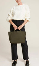Load image into Gallery viewer, Woman standing holding Naghedi handwoven neoprene St. Barths Medium Tote bag in Olive green, available at Amara Home.