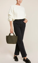 Load image into Gallery viewer, Woman standing with Naghedi handwoven neoprene St. Barths Small Tote bag in Olive green, available at Amara Home.