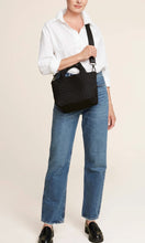 Load image into Gallery viewer, Woman standing with Naghedi handwoven neoprene St. Barths Small Tote bag in Onyx, available at Amara Home.
